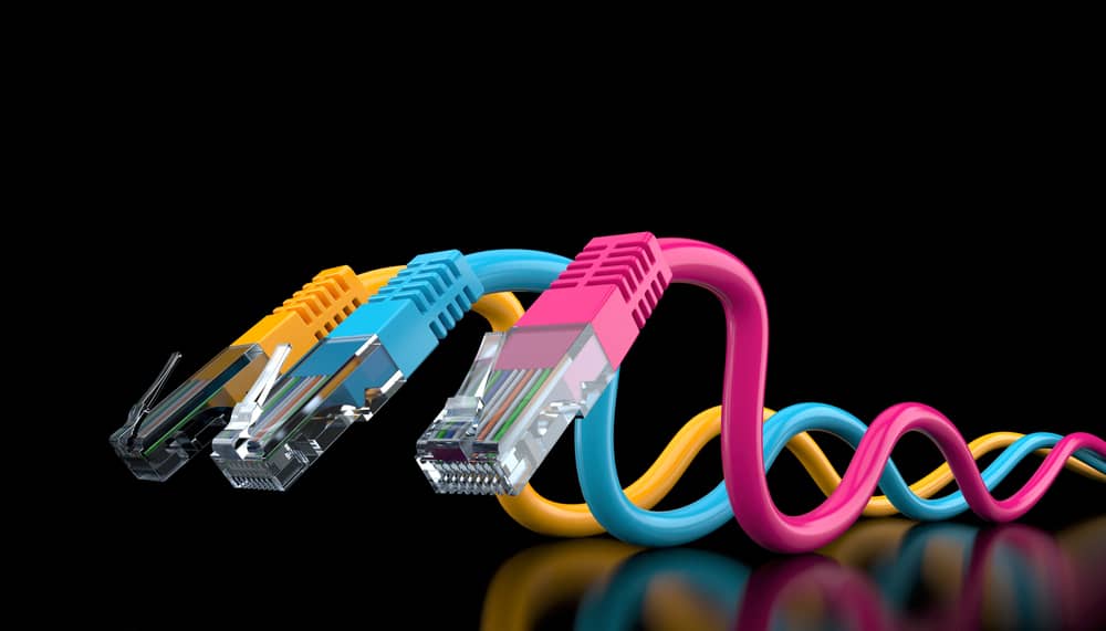 Tres conectores RJ-45 de colores sobre fondo negro. Imagen muestra cables de red con conectores RJ45. Tecnología de redes.